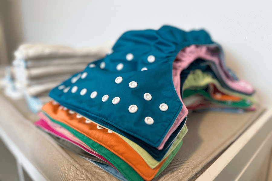 stack of cloth diaper shells on a changing table - cloth diapering tips