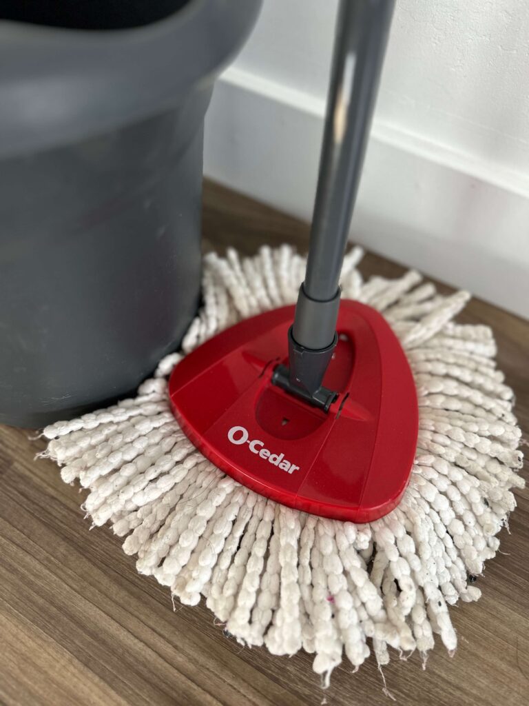 picture of a red ocedar mop with a white microfiber mop head and a dark grey mop bucket next to it.