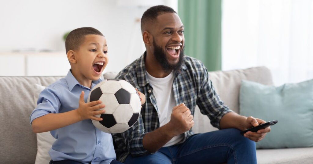 toddler fathers day gifts. son and father sitting on the couch watching soccer