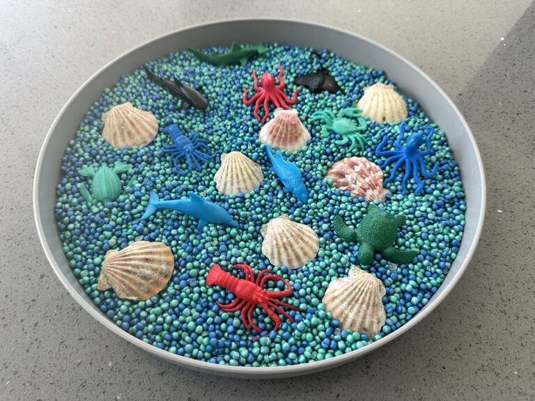 ocean sensory bin for toddlers with seashells, ocean animals, and a couscous sensory play base
